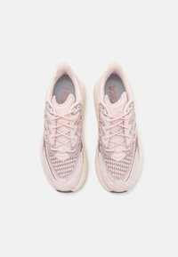 Zapatillas de correr de color rosa claro con parte superior de malla texturizada, cordones reforzados, collar acolchado y suela acolchada, con una marca sutil en la lengüeta.