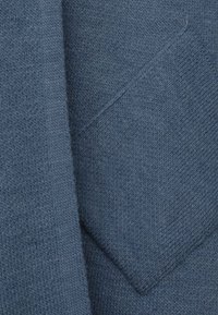 Sweter z miękkiego, teksturowanego niebieskiego materiału, z kieszonką na łatkę. Design przedstawia gładki wzór dzianiny oraz luźny krój.