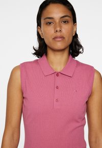 Pikétröja i ljusrosa, ärmlös design, med krage och tre knappar. Diskreta mönstrade detaljer på axlarna.