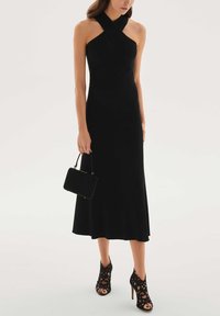 Fekete bordázott midi ruha átlapolt halter nyakrésszel, hozzá egy kis fekete kézitáska és bonyolult, fekete kivágott magas sarkú cipők.