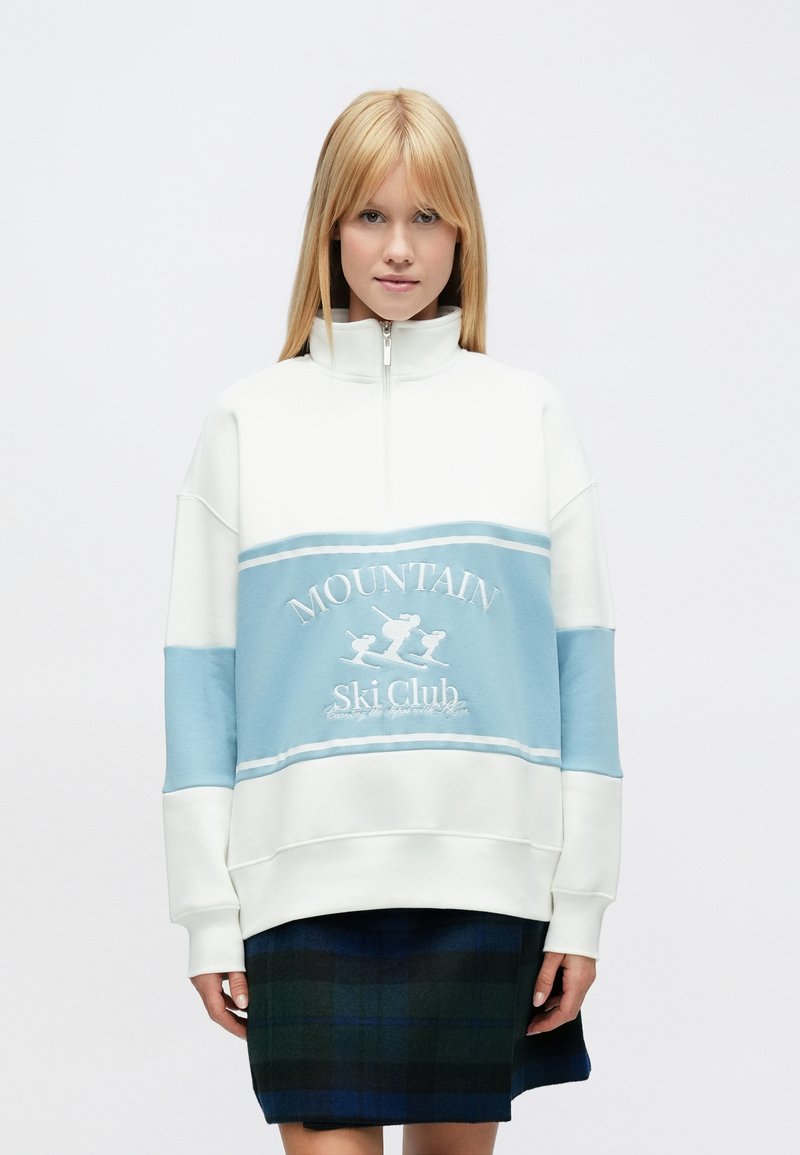 Valge ja heleroheline lukuga dressipluus, millele on tikitud "MOUNTAIN Ski Club", laiad varrukad ja lõdvestunud lõige.