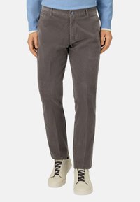 Pantalones de pana grises con estrías horizontales, diseño ajustado, bolsillos frontales, parte delantera plana y cierre de botón. Combinados con zapatillas ligeras.