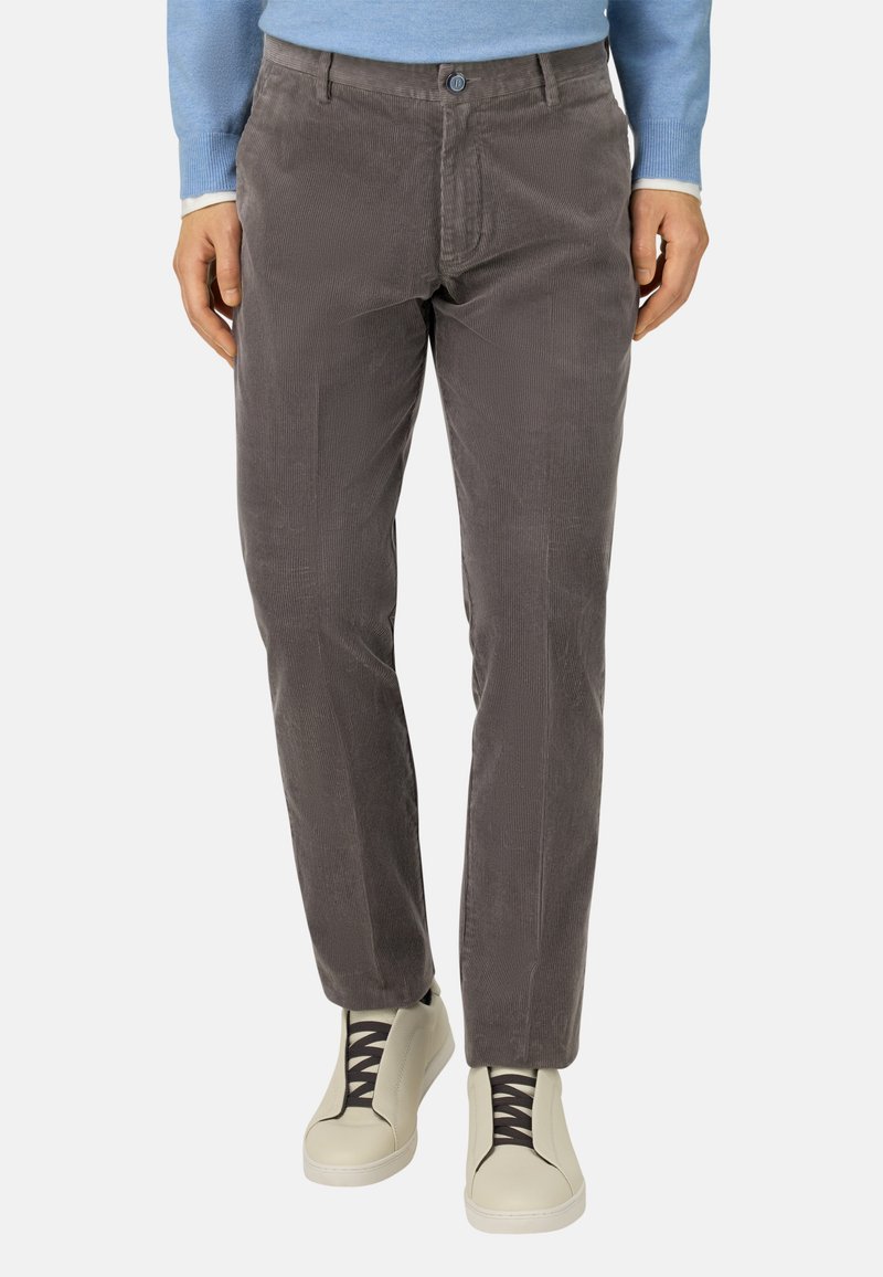 Pantalones de pana grises con estrías horizontales, diseño ajustado, bolsillos frontales, parte delantera plana y cierre de botón. Combinados con zapatillas ligeras.