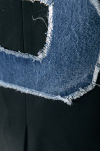 Denimist laik, millel on narmendavad servad musta tekstiili taustal, millel on silmatorkav lõigatud kuju. Tekstuuride kontrast erinevate materjalide vahel.