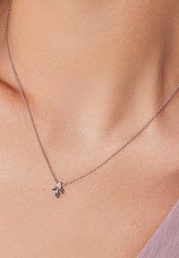 Srebrny naszyjnik łańcuszkowy z małym kwiatowym wisiorkiem z liśćmi i centralnym kamieniem. Noszony na szyi o gładkiej skórze.