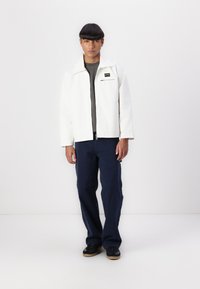 White zip-up jacket with lapel, gray shirt underneath, navy cargo pants, and black sneakers; minimalistic design, smooth texture, casual fit.