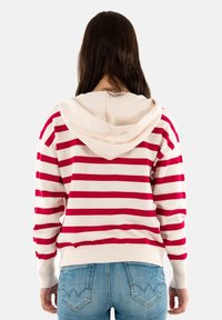 Haut à capuche rayé rouge et blanc avec une texture douce et une taille ajustée, featuring une capuche et des manches décontractées, assorti à un jean bleu.