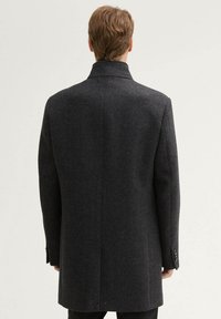 Cappotto in lana grigio scuro con design sartoriale, taglio dritto e colletto a revers. Presenta accenti in bottone sui polsini. Vista posteriore semplice.