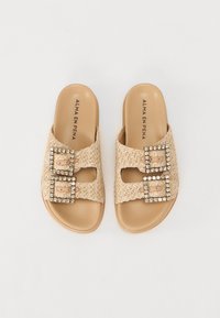 Beige glidesandaler med vevd overdel, som har to firkantede spenne dekorert med krystaller. Kontrollert innersåle og flat design.
