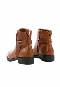 Stivali ankle in pelle marrone con punta rotonda e tacco basso a blocco. Le caratteristiche includono una zip laterale e un dettaglio a fiocco decorativo sul retro.