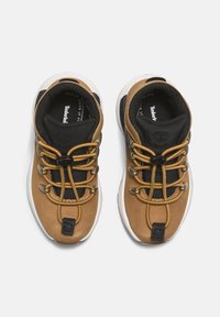Braune Leder- und schwarze Mesh-Sneaker mit weißen Sohlen, ausgestattet mit braunen Schnürsenkeln, metallischen Beschlägen und einem abgerundeten Design. Timberland-Logo sichtbar.