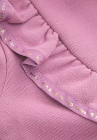 Tejido rosa claro con punto texturizado. Presenta detalles con volantes y una cinta con logo en letras doradas que dice "TED BAKER BY TED BAKER."