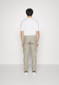 Béžové cargo kalhoty se bočními kapsami a rovný střih, zkombinované s jednoduchým bílým tričkem, z pohledu zezadu. Měkký bavlněný materiál.