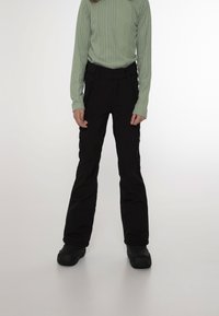 Pantaloni da neve neri a lunghezza ginocchio con vita aderente e gambe dritte, dotati di tasche con zip e una texture opaca. Abbinati a un maglione verde chiaro.