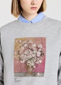 Felpa grigia con un'opera d'arte stampata di rose rosa in un vaso su uno sfondo testurizzato. L'etichetta include l'artista e i dettagli.