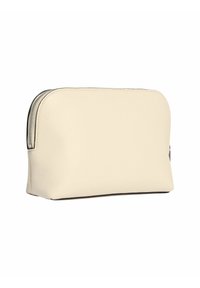 Borsa di pelle color crema con una parte superiore arrotondata, superficie testurizzata, cerniera nera e un sottile dettaglio del logo sul lato. Design compatto.