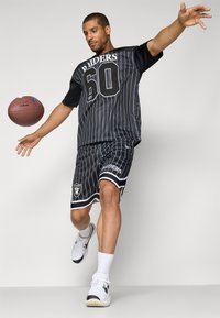 Black and white striped sports outfit with a short-sleeve top and shorts. Features a logo, number 60, and white accents. Model holding a football.