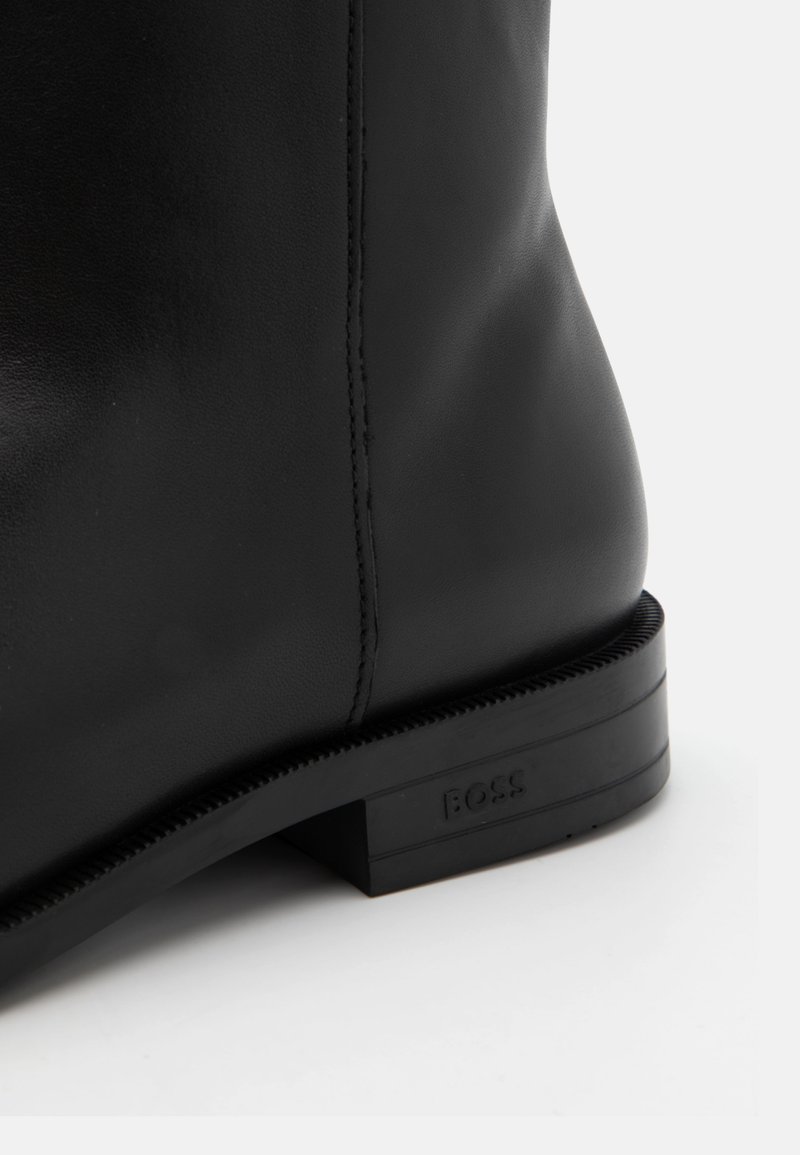 Bottine noire en cuir au fini lisse, avec des coutures discrètes et un petit talon en caoutchouc, arborant le logo "BOSS" sur le côté.
