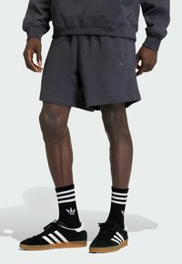 Donkergrijze katoenen shorts met een elastische tailleband, gecombineerd met zwarte Adidas schoenen met witte strepen en bijpassende zwarte sokken met strepen.