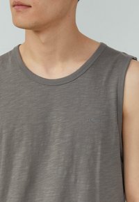 Lichtgrijze tanktop met een ronde halslijn en mouwloos ontwerp. Beschikt over een subtiele textuur en een klein geborduurd logo op de borst.