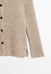 Beige stickad kofta med ett strukturerat mönster, utrustad med svarta knappar, sidoflikar och långa ärmar. Materialet verkar mjukt och andningsbart.