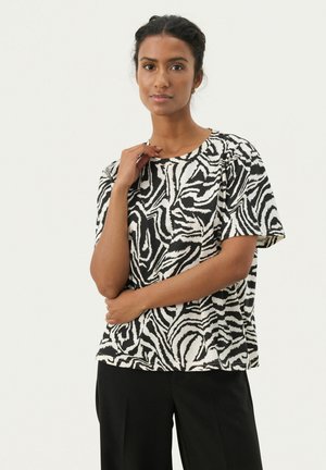 T-shirt à imprimé zèbre noir et blanc, à manches courtes, col rond, texture douce, coupe décontractée, associé à un pantalon noir.