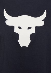 Vit stiliserad tjurhuvudgrafik med framträdande horn och ögon centrerad på en mörk tygbakgrund.