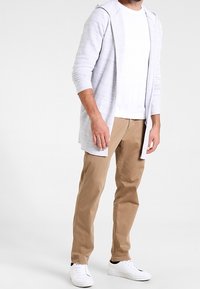 Lysegrå lang cardigan med hætte, hvid t-shirt, beige chinos og hvide sneakers. Cardiganen har tekstureret stof og åben front.