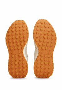 Suole delle scarpe con una base in gomma arancione texturizzata con un motivo esagonale, logo in rilievo sul lato e bordo superiore color crema.
