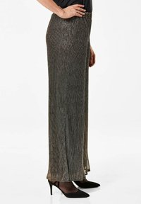 Metallic geplooide maxi rok in donkere tinten, met een gestructureerde afwerking en een verlengde vorm, gecombineerd met zwarte hakken.