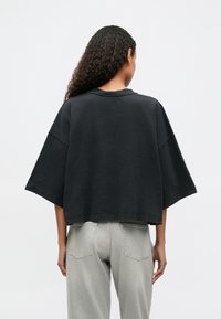 Fekete pamut, oversized póló kerek nyakkivágással és rövid ujjakkal, világosszürke, magas derekú farmernadrággal párosítva.