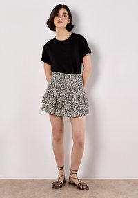 Camiseta negra de cuello redondo combinada con una falda corta de capas con un estampado animal en beige y negro. Participante lleva sandalias con tiras.