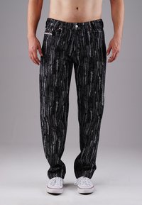 Schwarze Hose mit einem strukturierten, abstrakten Muster in Grau. Verfügt über einen elastischen Bund und zwei Fronttaschen, kombiniert mit weißen Sneakers.