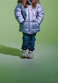 Kurtka puchowa w jasnym fioletowym kolorze, z pikowanymi liniami i guzikami; zestawiona z luźnymi niebieskimi dżinsami i białymi trampkami z szarymi akcentami.