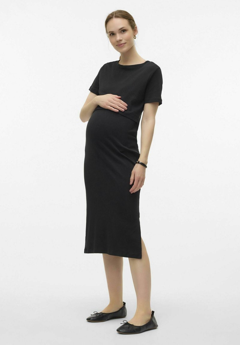 Robe de maternité noire à côtes avec des manches courtes, taille ajustée, longueur au genou, accompagnée de ballerines noires. Texture lisse et douce.