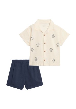 Kurzärmliges cremefarbenes Hemd mit schwarzen Vogelmotiven und Holzknöpfen, kombiniert mit dunkelblauen Shorts mit elastischem Bund.