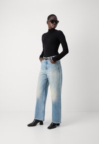 Un haut noir à manches longues, un jean large bleu clair avec une texture délavée, des bottines noires à talons et des lunettes de soleil noires surdimensionnées.