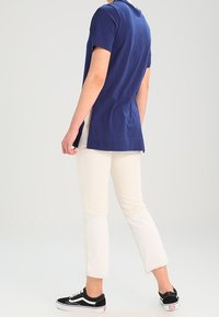 Marinblus kortärmad skjorta med rak skärning, som matchas med beige caprijeans med fransade fållar och svarta kanvas sneakers.