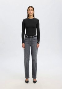 Črna majica z dolgimi rokavi, sive kavbojke s pasom in ravnimi nogami ter črne čevlje z ostrim koncem. Gladek material, minimalni detajli, oprijeta silhueta.