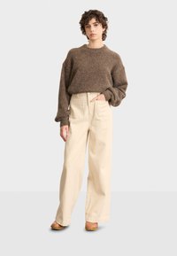 Maglione marrone dalla texture morbida con maniche larghe, abbinato a pantaloni beige a gamba larga con vita alta e zoccoli marroni con tacco.