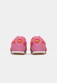 Rosa og orange ruskinds sneakers med en hvid sål, der har et gult logo, strukturerede paneler og kontrasterende striber på hælen.