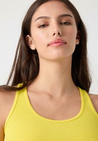 Top de tirantes amarillo con cuello redondo, que presenta un diseño ajustado y una textura suave. La tela parece ligera y elástica.