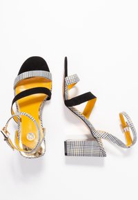 Svart och vit rutig klacksandaler med fyrkantig blockklack, flera remmar och en ljusgul innersula. Tillverkade av strukturerad mocka.