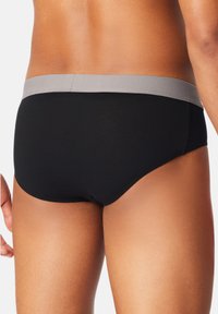 Caleçons noirs avec une ceinture élastique grise, texture lisse et coupe ajustée, affichant une forme contournée et des coutures minimes.