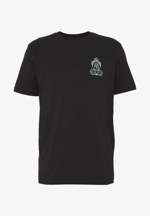 T-shirt en coton noir avec un col rond et un design graphique sur le devant, assortie à un jean en denim clair et des baskets blanches.