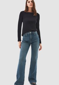 Top nero a maniche lunghe con scollatura rotonda abbinato a jeans svasati azzurri chiari. I jeans presentano un classico design a cinque tasche.