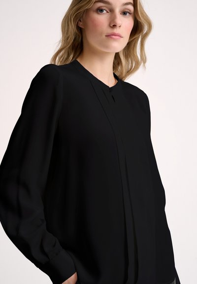 Blusa nera con scollo rotondo e maniche lunghe, caratterizzata da un dettaglio con piega frontale. Tessuto morbido con un taglio leggermente loose.