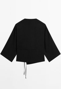 Veste noire à manches longues avec des manches larges, ourlet asymétrique et deux liens suspendus au centre à l'arrière.