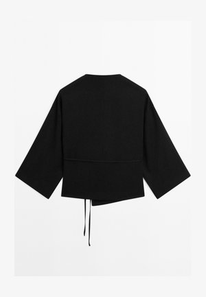 Veste noire à manches longues avec des manches larges, ourlet asymétrique et deux liens suspendus au centre à l'arrière.