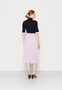 Top preto justo com mangas curtas, combinado com uma saia midi lilás fluida. O modelo usa sandálias pretas de salto bloco.